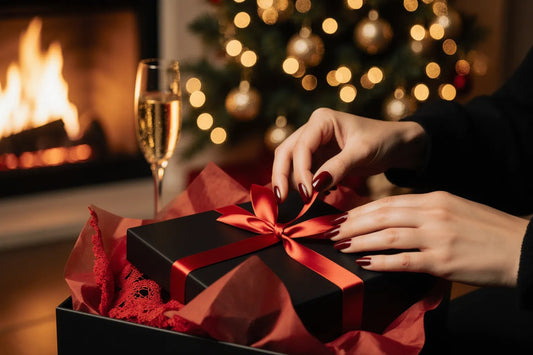 Manos desatando el lazo rojo de una caja de regalo con lencería junto al árbol de Navidad